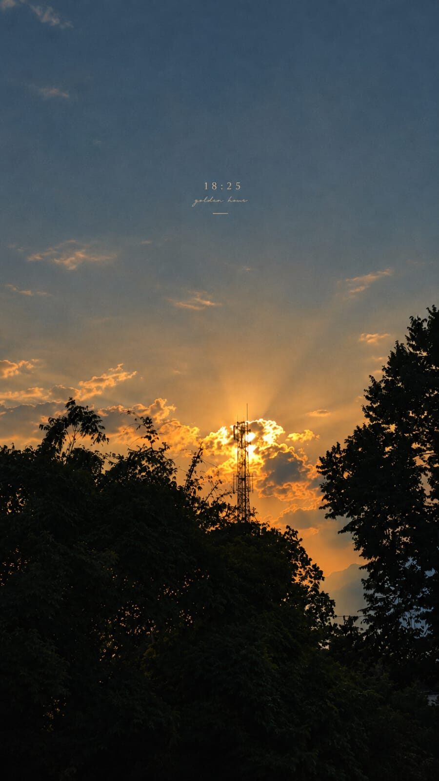 Photograph of a sunset behind trees, golden hour light rays through the clouds