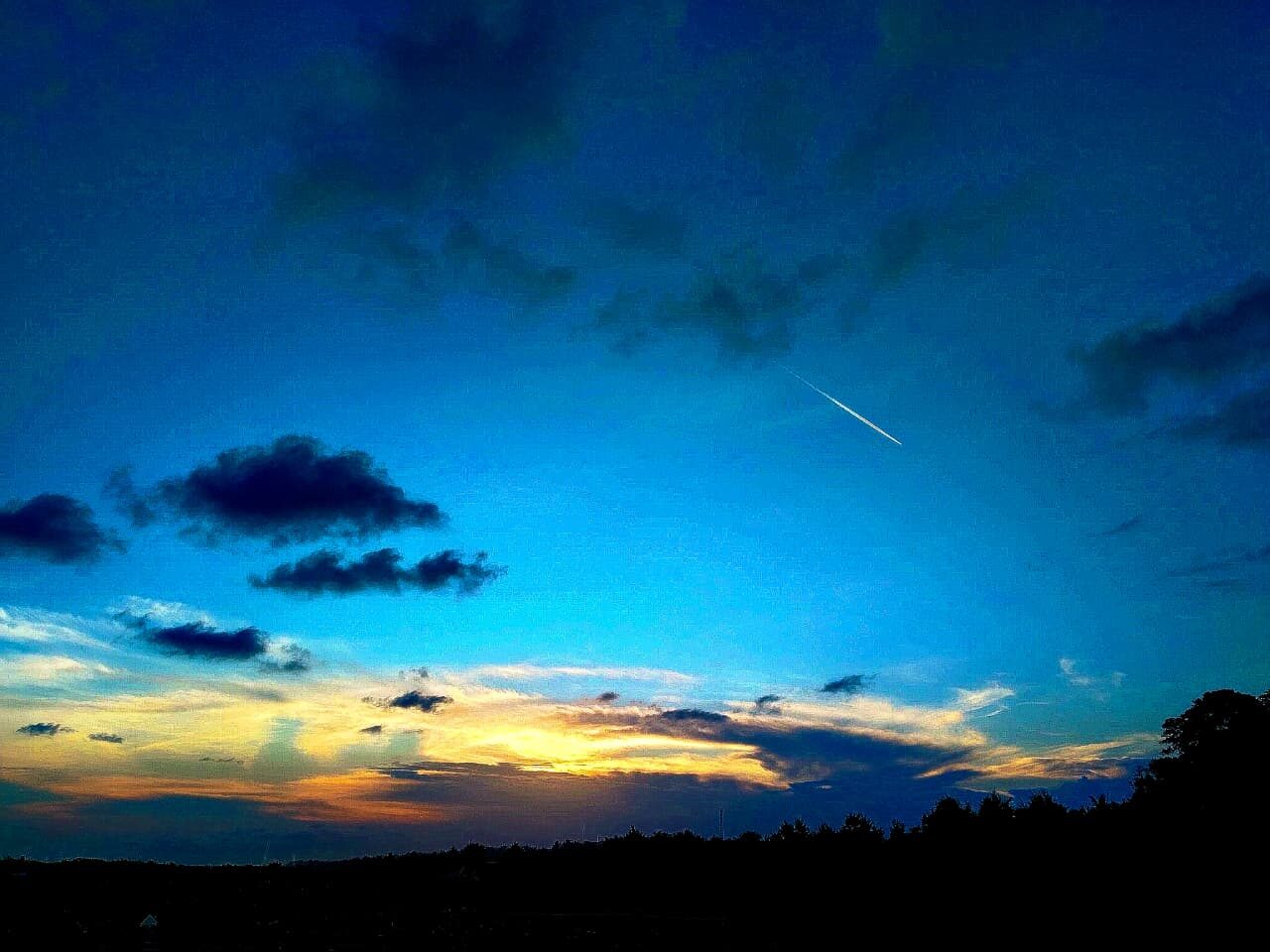 Photograph of a blue dusk sky with a jet contrail and glowing horizon