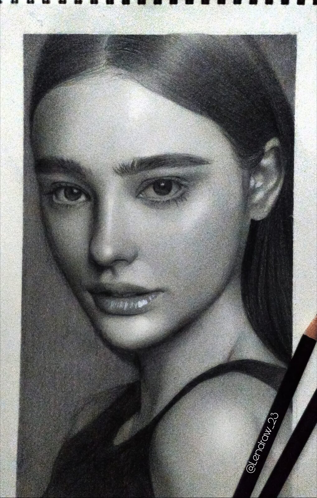 Black and white graphite portrait drawing with pencils resting beside it